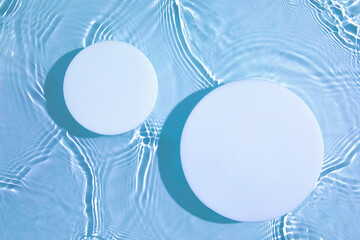 Two empty white circle podium on transparent clear calm blue water texture with splashes and waves...