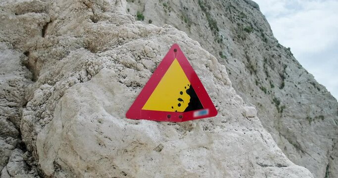 Warning sign of landslide danger on a stone with tall cliff on background.