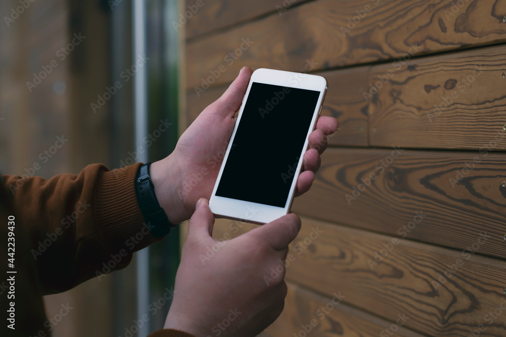 Poster man holds a mock-up of a smartphone with a black screen in his hands on a wooden background.