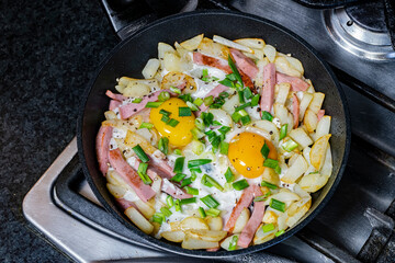 Traditional homemade fried eggs with potatoes and sausage in a frying pan