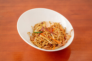 White bowl of sauteed noodles with fresh vegetables and yakisoba sauce on orange table