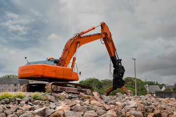 Red excavator with rock or stone grab attached to the arm. Heavy machinery equipment on a construction site