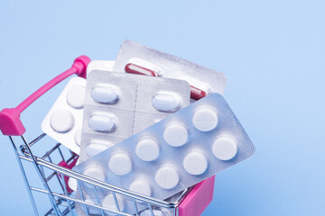 A variety of pills in blister packs in a mini shopping trolley on a blue background. Health and...