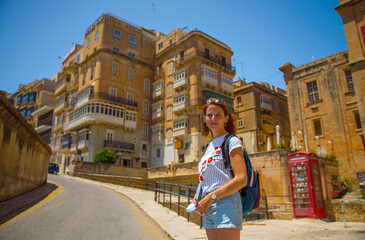 Valletta, Malta. Beautiful tourist woman looking at the camera. Old historic street in Malta - travel photography. Traditional Maltese architecture. Old historical part of Valetta.
