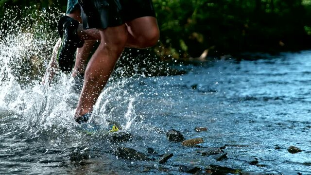 Super slow motion of legs of a runner in sneakers splashng in forest stream. Filmed on high speed cinematic camera at 1000 fps.
