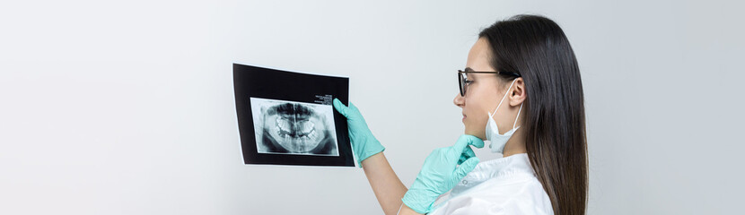 Girl dentist in a white coat holds a snapshot of the patient's teeth.