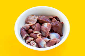 Mixed chicken entrails in white bowl on yellow background.