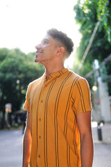 Young gay latino man wearing a yellow striped shirt with clipping light and trees in the background