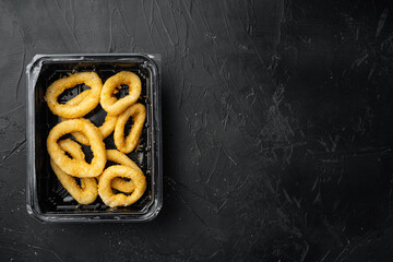 Raw crispy squid rings in breadcrumbs package, on black dark stone table background, top view flat...