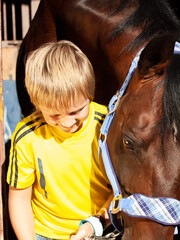 happy  portrait  of little boy with horse posing in stable. sunny day