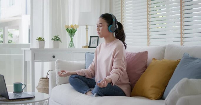 Young asia people teenage girl close eyes sit on sofa couch at home easy asana lotus pose in yoga app zen online class on internet on break time self relax calm, rest mind and mental health life care.