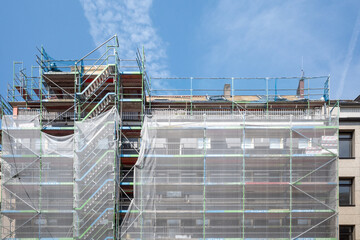 Front exterior view of net wrap scaffolding in front of building at construction site. - obrazy, fototapety, plakaty