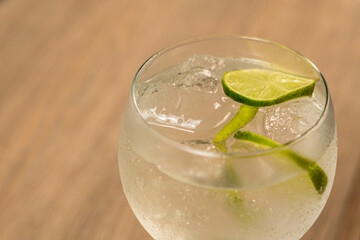Close-up of a gin and tonic cocktail with a slice of lemon against the light.