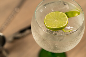 Close-up of a gin and tonic cocktail with a slice of lemon and out-of-focus implements.