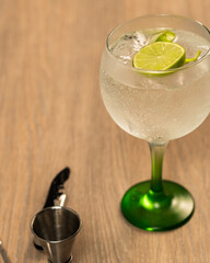 Front view of gin and tonic with lemon and jigger on wooden surface
