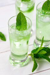 Summer Sweet Refreshing Mint Liqueur Cocktail Shots with Ice and Mint Leaves on White Wooden Background. Selective focus.