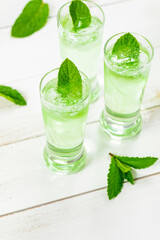 Summer Sweet Refreshing Mint Liqueur Cocktail Shots with Ice and Mint Leaves on White Wooden Background. Selective focus.