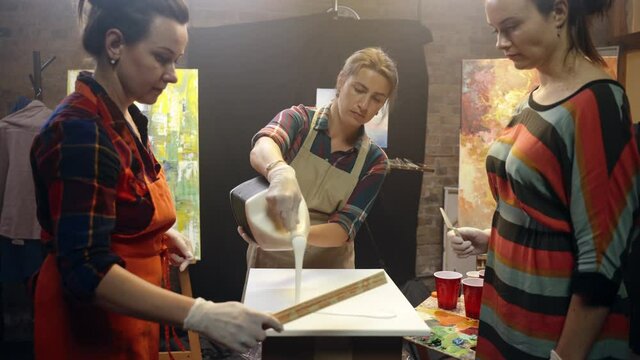 Women artists pouring white glue on the canvas. Artistic collaboration in workshop.