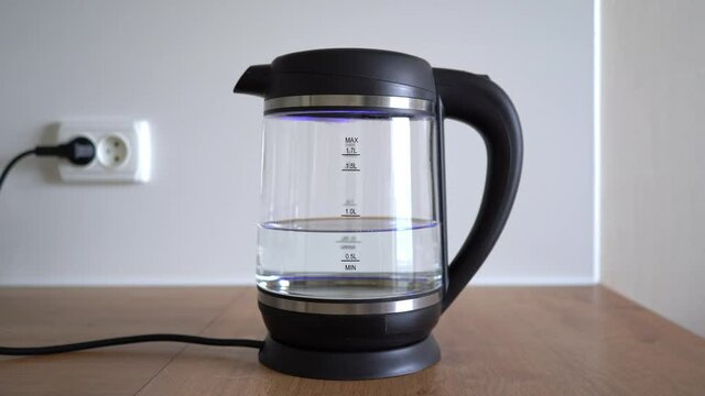 Seething water with bubbles boils in transparent glass electric kettle. Man boiling water in an electric kettle on white background. 4k stock footage.