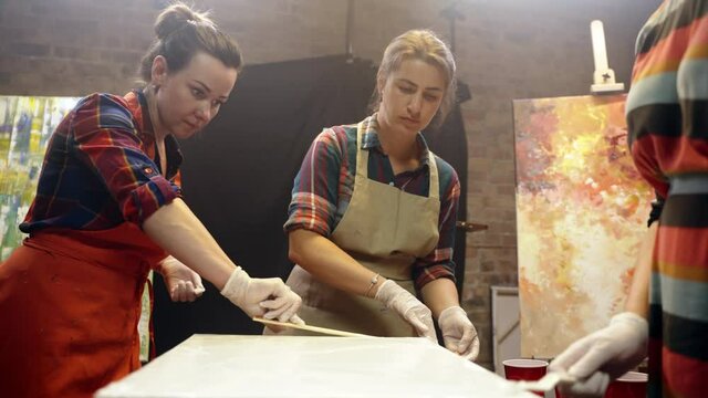 Women artists smering white glue on the canvas. Artistic collaboration in workshop.