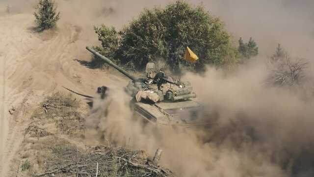 Tank driving in sand dunes close up aerial view. Military army training. Drone back view armoured combat fighting vechicle moving in dust clouds. The gunner controls the muzzle. War battle technology.