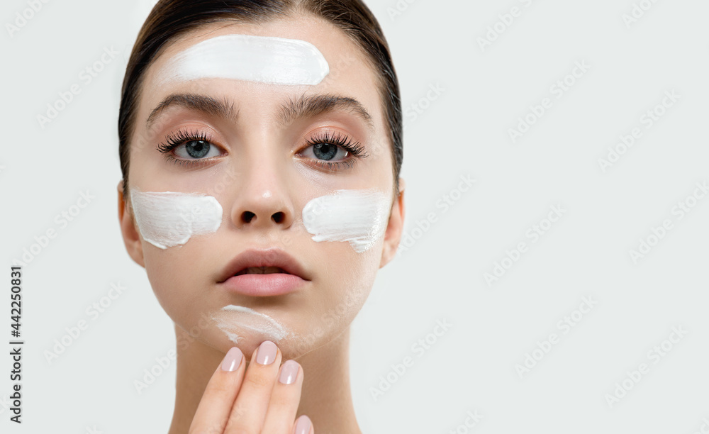 Wall mural young woman applying face cream or facial mask at her face. beauty model with perfect fresh skin and