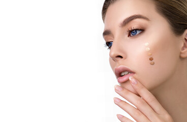 Young woman applying five color samples of facial foundation cream or corrector at her face. Beauty model with perfect fresh skin and long eyelashes cares about her skin at home.