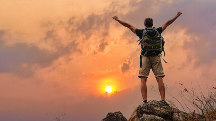 hiker with trekking stick hiking success on rocky hill top at sunset sky