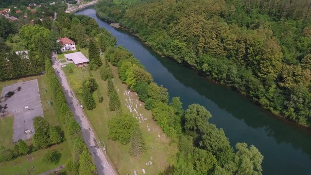 A drone flight over a scenic view of an ancient graveyard and a river and main road that follows its course.