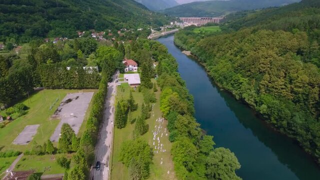 A drone flight over a scenic landscape view with an ancient graveyard and a river and main road that follows its course heading to the hydroelectric power plant.