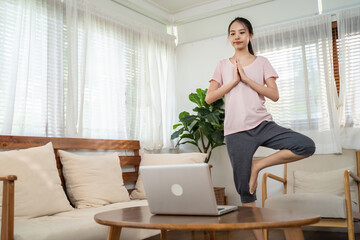 Asian young girl doing Yoga, follow online trainer in laptop at home.