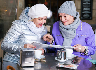 Fototapeta na wymiar Happy mature ladies travellers relaxing at cozy outdoor cafe and looking map