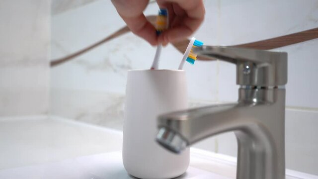 Picture of adult's hand which taking one toothbrush from plastic glass which standing near washbasin. 4k stock footage.