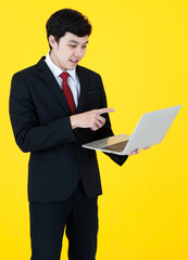 Vertical portrait shot of young adult Asian handsome man in a black long sleeve suit holding a laptop while touching the screen isolated with a yellow background in studio. Concept of video conference