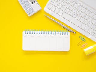 Flat lay of office yellow desktop with blank monthly notebook and keyboard, pen with stationery equipment. Top view with space for text. Business and education concept.