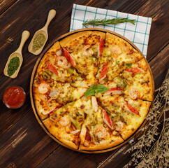 Banner of homemade seafood pizza with shrimp, crab sticks, bell peppers topping on wooden tray, table, decorated by tomato sauce, ketchup, oregano ingredients with napkin in kitchen and copy space.