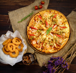 Vertical photo and close up on tasty homemade seafood pizza on sackcloth with dried flowers, cold beverage, Fried onions on wooden table. Food and Beverage Concept.