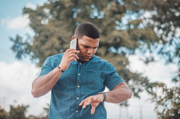 young dominican latin businessman talking on mobile phone in the park and watching his watch.