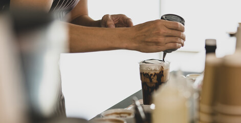 Unrecognizable  barista man smiles and happy as enjoy decorating creamy foam of cold drinks in plastic cup with elaborate by squeezing bottle to pour chocolates on it