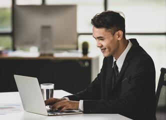 Naklejka na ściany i meble Cheerful businessman typing on laptop in office