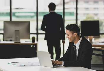 Asian man working on laptop in office with colleague