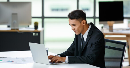 Fototapeta na wymiar Cheerful businessman typing on laptop in office