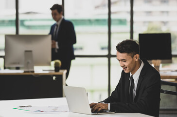 Asian man working on laptop in office with colleague
