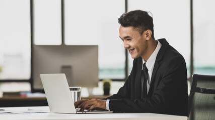 Cheerful businessman typing on laptop in office