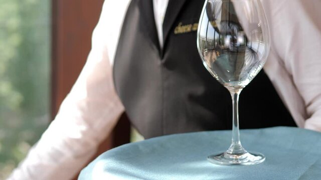 Table setting in an elite restaurant close-up. Men's hands arrange beautiful clean and empty glass glasses and plates from a tray. Decorative tableware and a candle holder. The waiter set the table