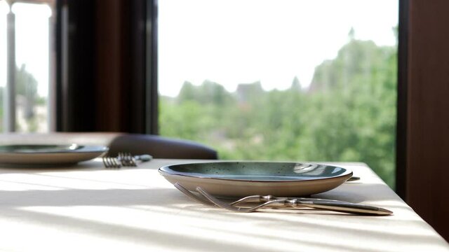 Waiter serves a table in an elite restaurant close-up. Men's hands arrange beautiful clean and empty glass glasses and plates.Decorative tableware and a candle holder.Restaurant with panoramic windows