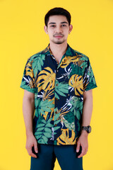 Fototapeta premium Handsome young Asian man in colorful Hawaiian shirt standing looking to camera. Half body studio portrait on yellow background. Relaxed and happy people in summer concept