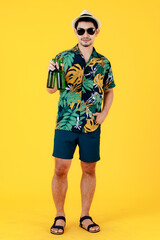 Joyful young Asian man with sunglasses smiling and raising a beer bottle. Full body studio portrait on yellow background. Cheerful and happy people in summer holidays concept.