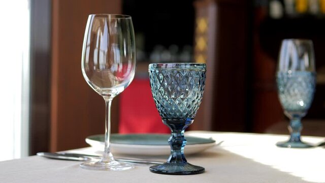 Table setting in an elite restaurant close-up. Men's hands arrange beautiful clean and empty glass glasses and plates. Decorative tableware and a candle holder. The waiter sets the table