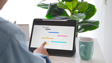 Man looking at time frame planner on digital tablet screen for mobile phone app delveloper team at...